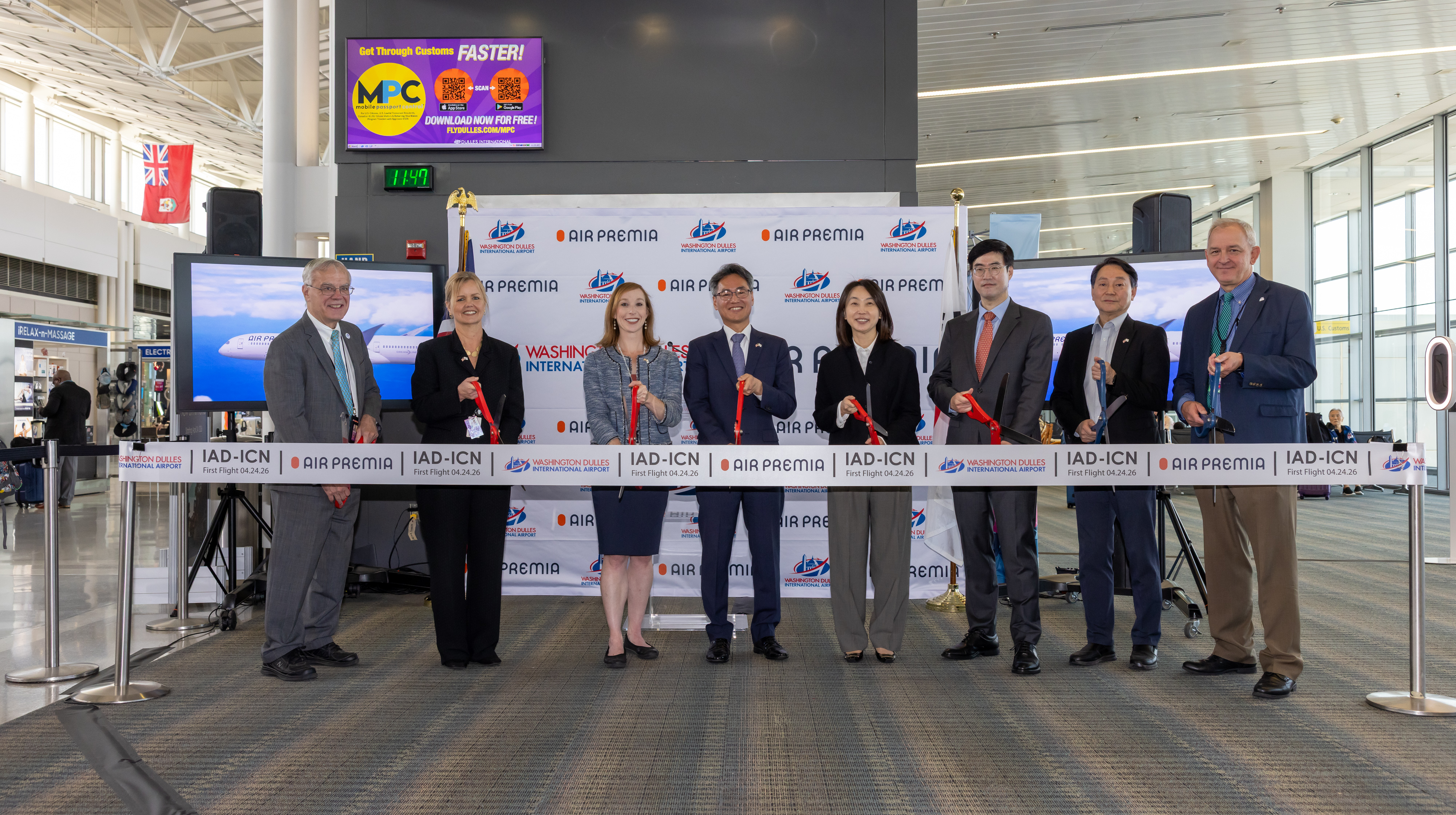 Eight people stand at a ribbon cutting for Air Premia at Dulles International
